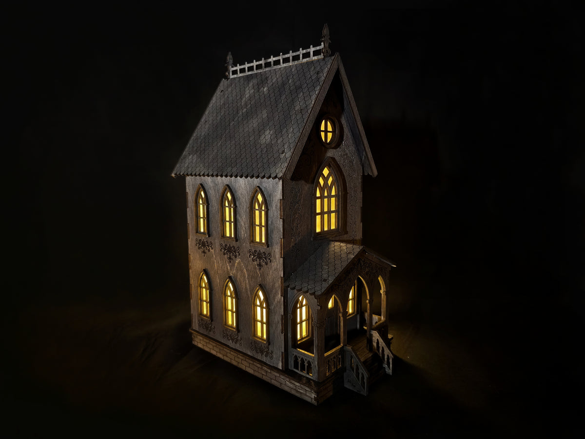 Svietiaci drevený gotický domček vyrezávaný laserom s teplým žltým svetlom v oknách ako halloweenska dekorácia