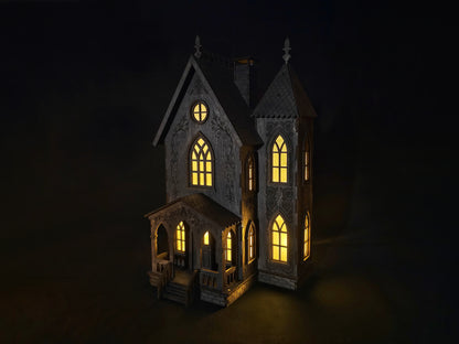 Svietiaci drevený gotický domček vyrezávaný laserom s teplým žltým svetlom v oknách ako halloweenska dekorácia